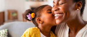 foto de uma menina dando um beijo na bochecha da sua mãe.